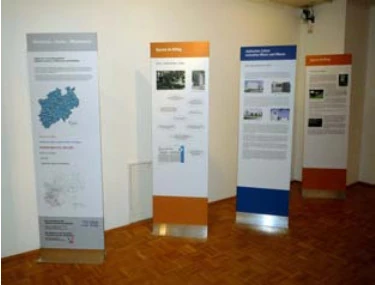 Es ist ein Ausstellungsraum zu sehen mit vier Aufstellern mit Bildern und Texten.