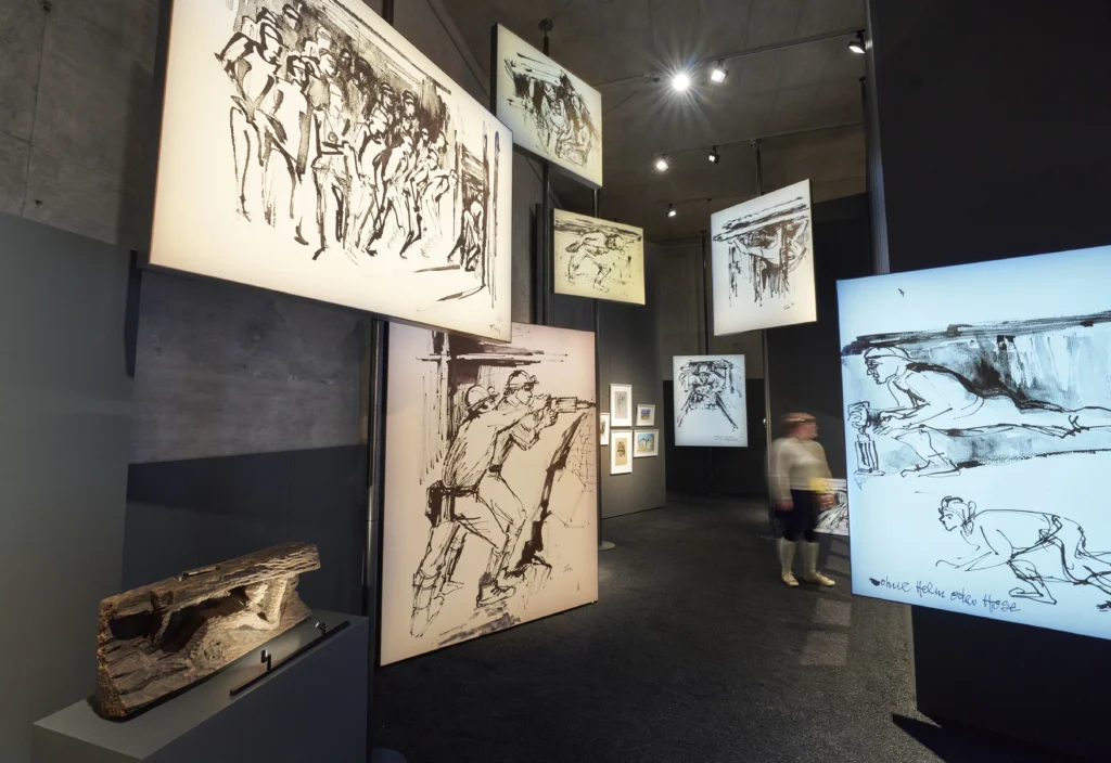 Ausstellungsbereich mit vielen vergößerten und beleuchteten Zeichnungen, die Bergarbeiter darstellen, die teils Untertage bei der Arbeit dargestellt werden.